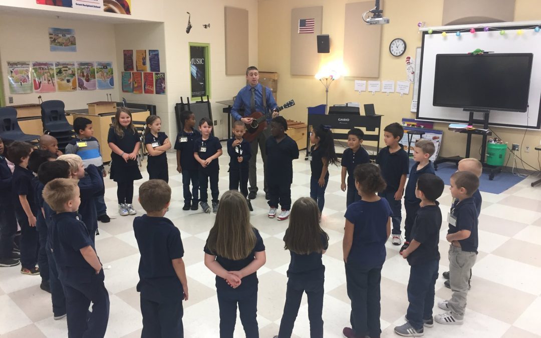 A group of children listening to Chris Martin playing guitar