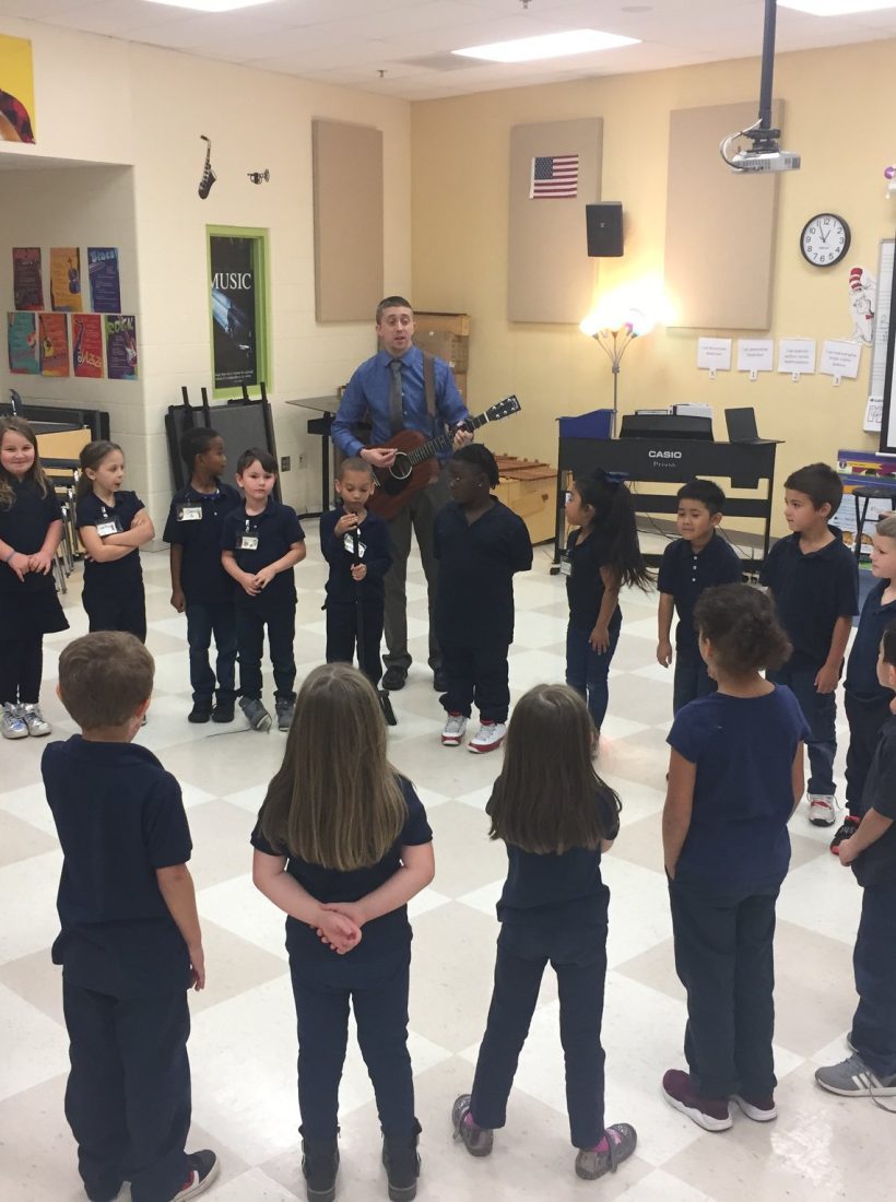 A group of children listening to Chris Martin playing guitar